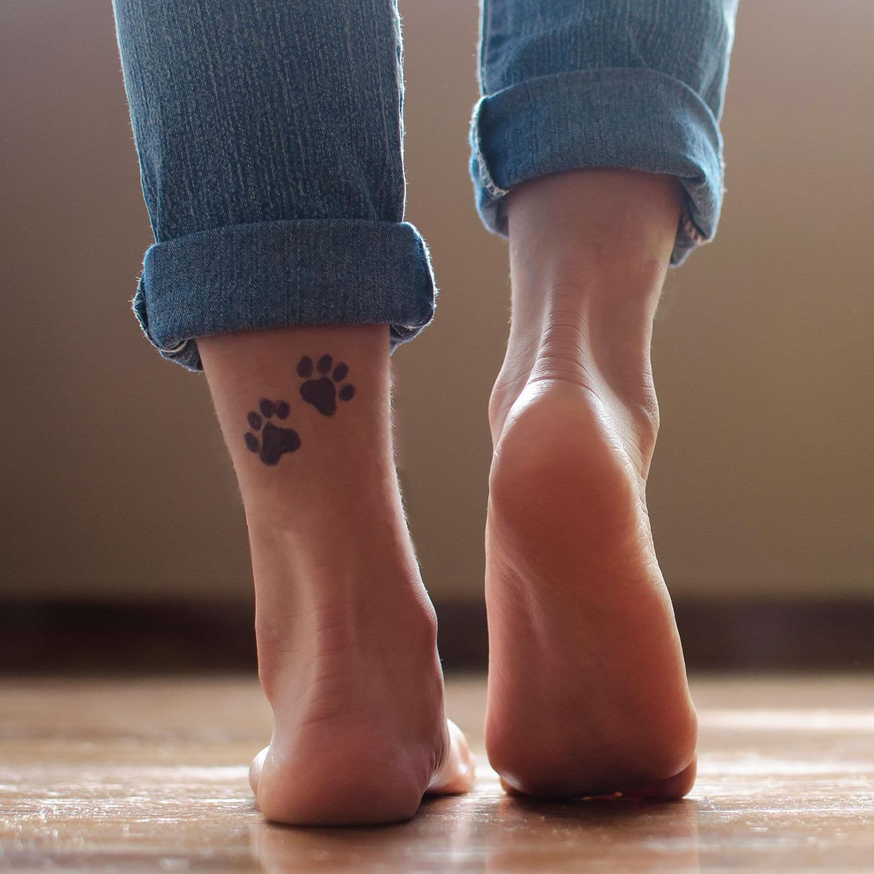 Nackte Fuess laufen auf einem Fliesenboden an der linken unteren Wade hat die Person 2 Pfoten taetowiert.