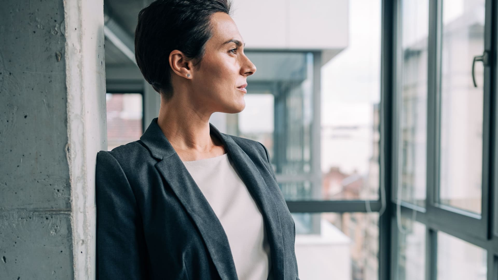 Eine Frau in Business Kleidung blickt aus dem Fenster eines Bürohochhauses.
