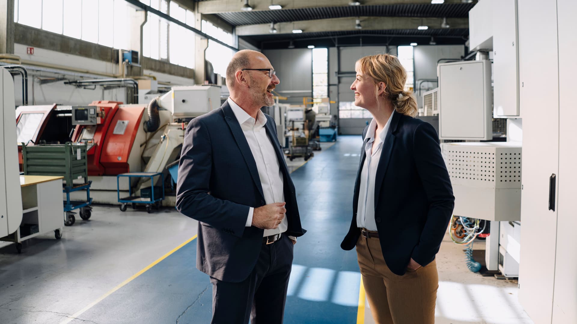 Geschäftsmann und Geschäftsfrau unterhalten sich in einer Fabrik und lachen dabei.