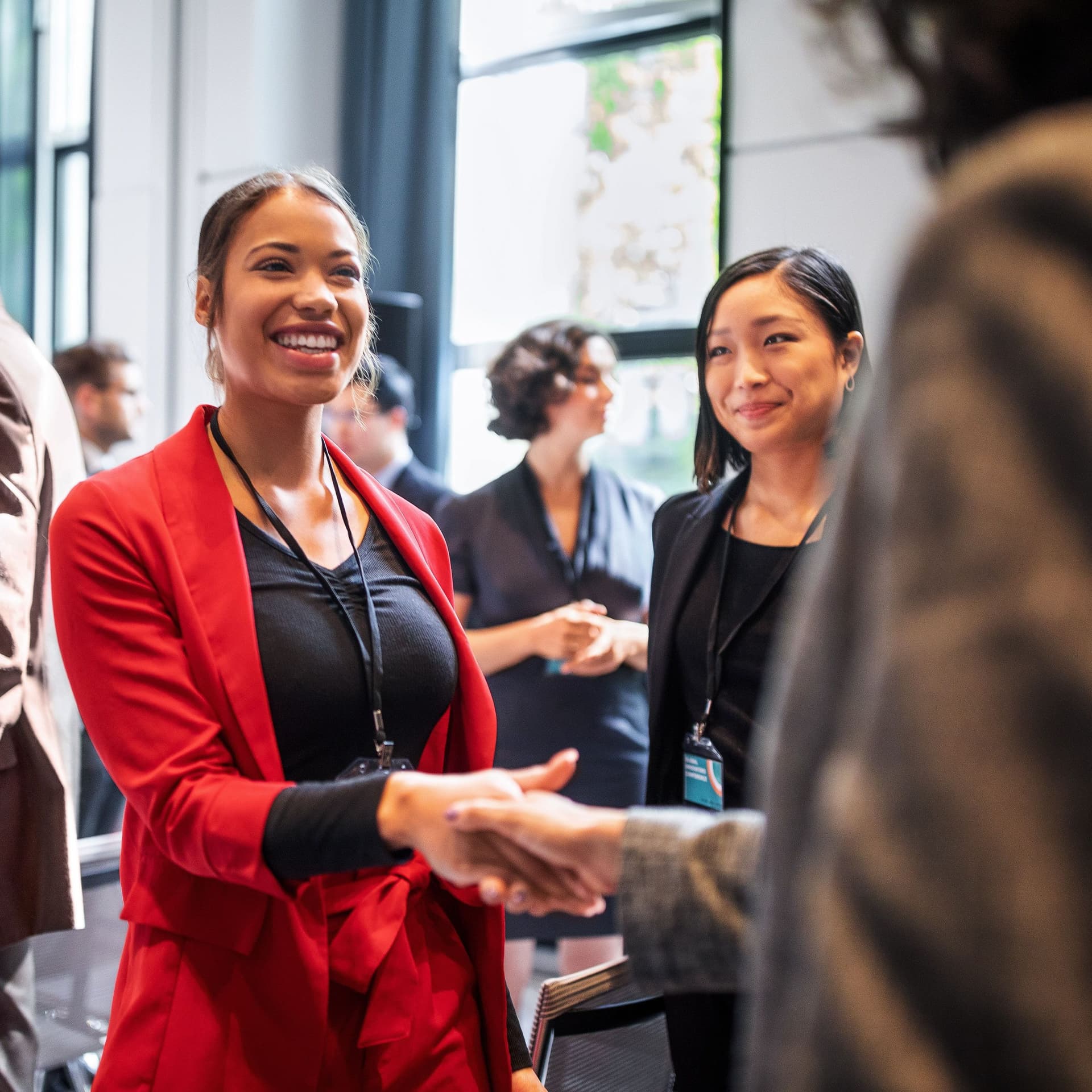 Selbstbewusste lächelnde Geschäftsfrauen beim Händeschütteln, während sie im Korridor eines Auditoriums stehen.