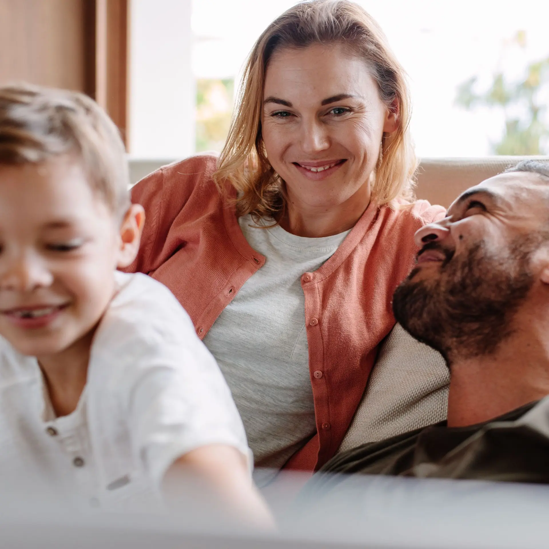 Eine junge Frau entspannt mit ihrem Mann und Sohn lächelnd auf einer Couch.