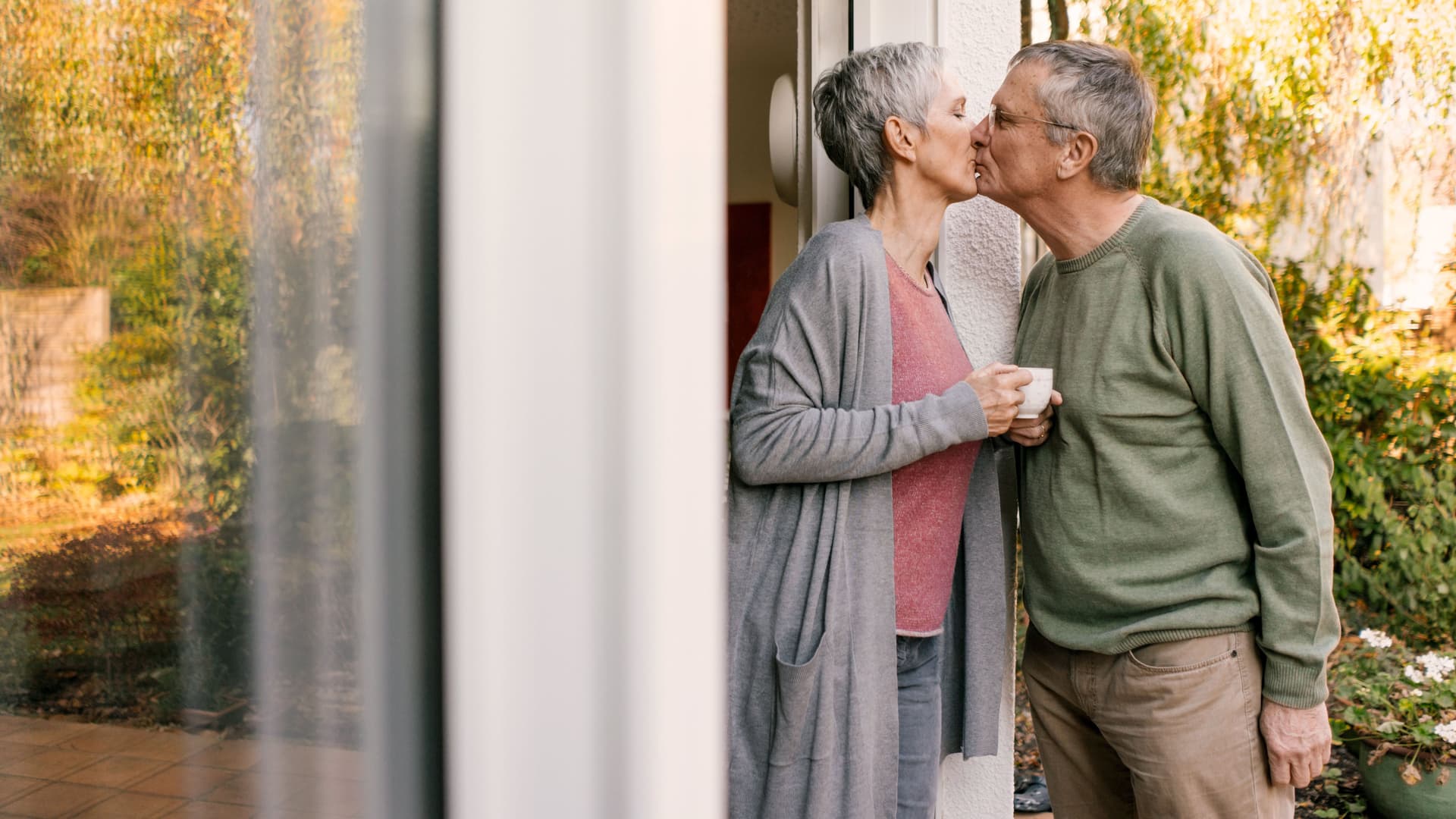 Älteres Paar küsst sich an einer Terrassentür.
