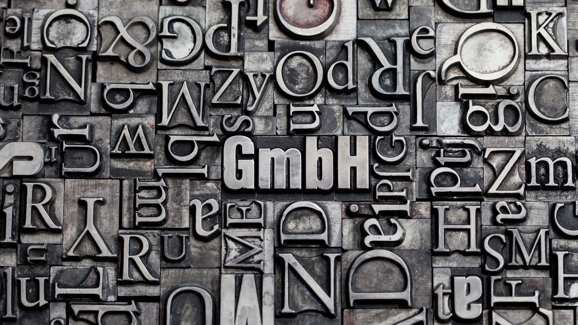 Verschiedene Setzbuchstaben aus Metall nebeneinander. In der Mitte steht GmbH.