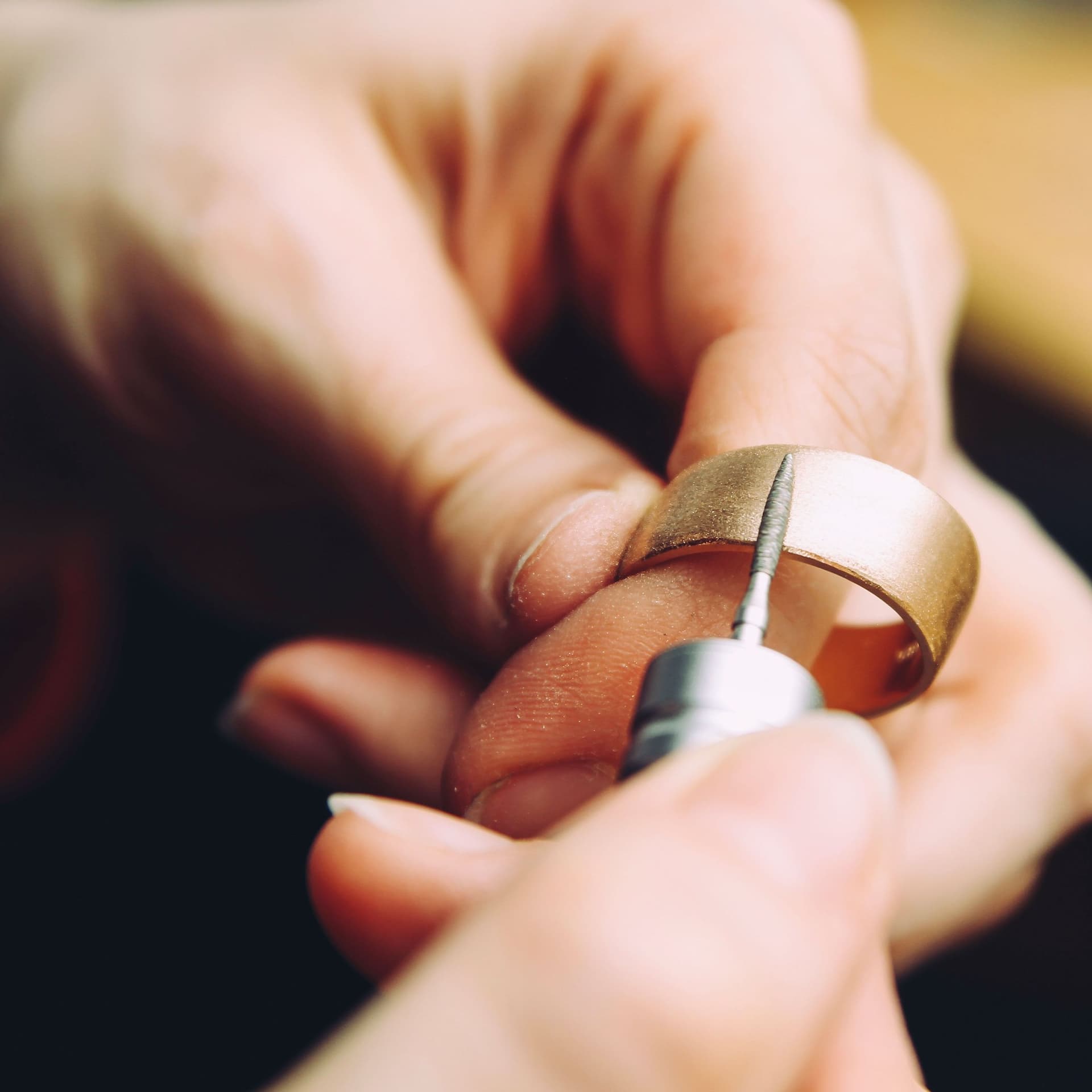 Nahaufnahme einer Hand und einem Goldring, der mit einem Diamantfräser bearbeitet wird.