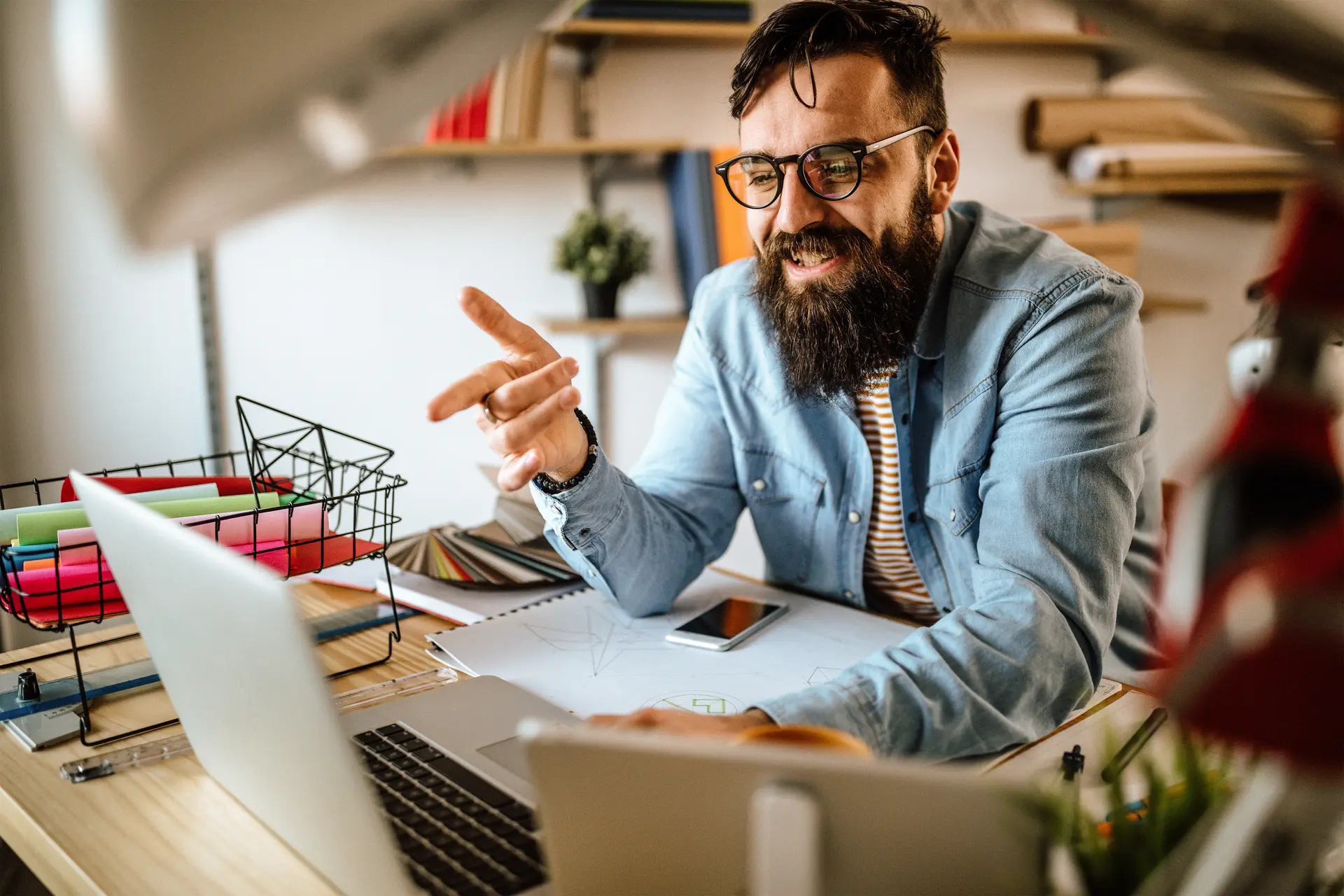 Foto eines lächelnden Mannes, der mit dem Finger auf einen aufgeklappten Laptop in einem Büro zeigt.