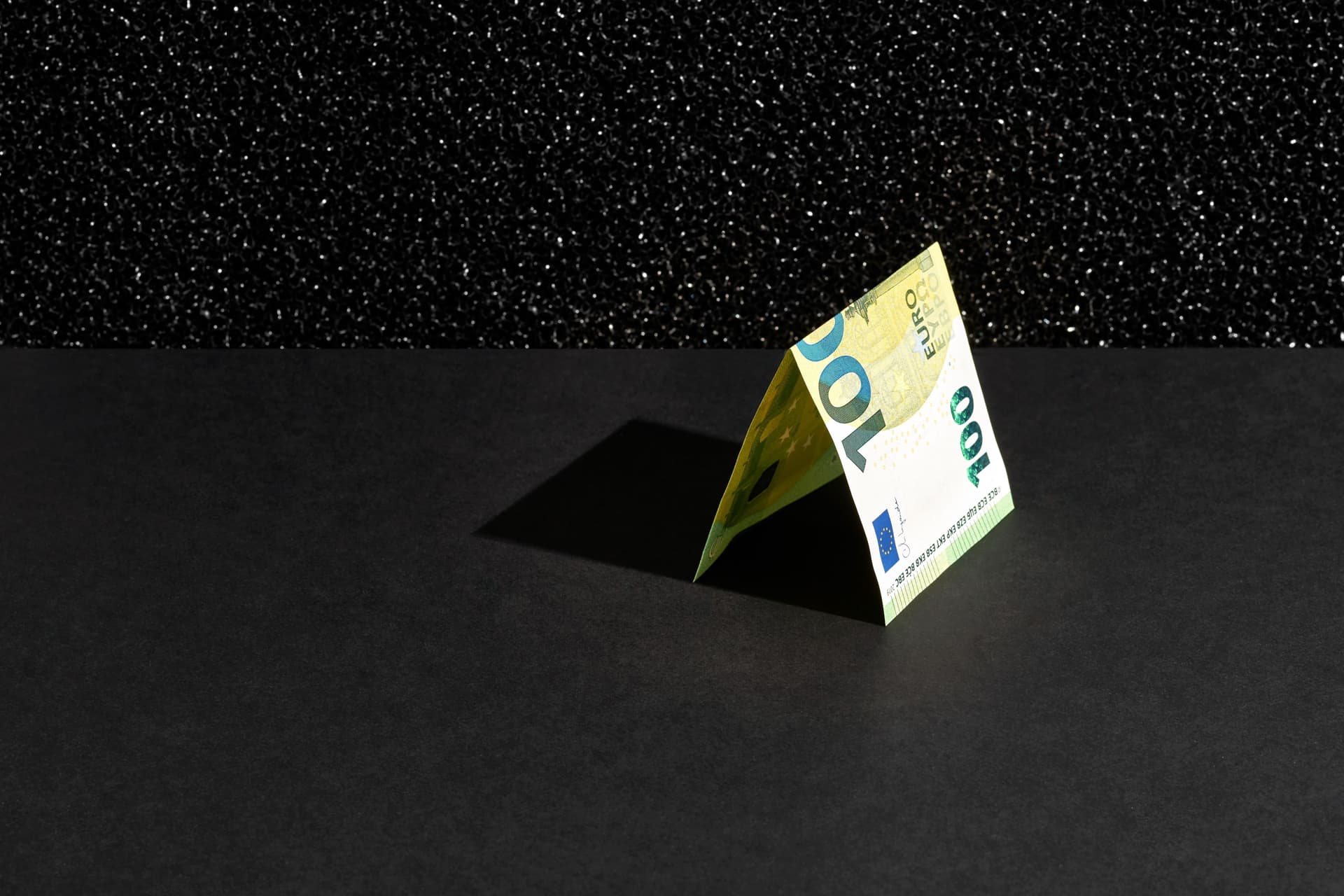 Ein 100-Euro Schein liegt gefaltet auf einem schwarzem Hintergrund.