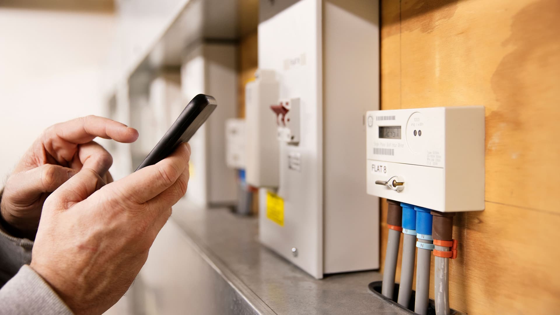 Eine Person liest mit dem Smartphone den Stromzähler in einem Technikraum ab.
