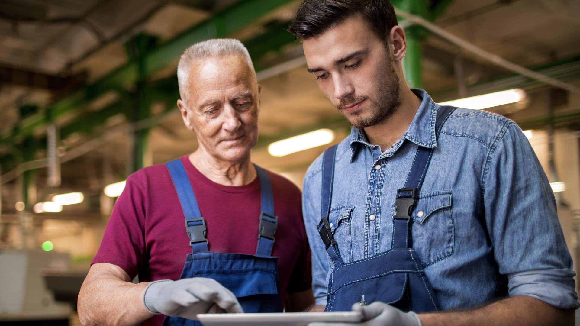 Zwei Männer in einer Fabrik, die auf ein Tablet schauen.