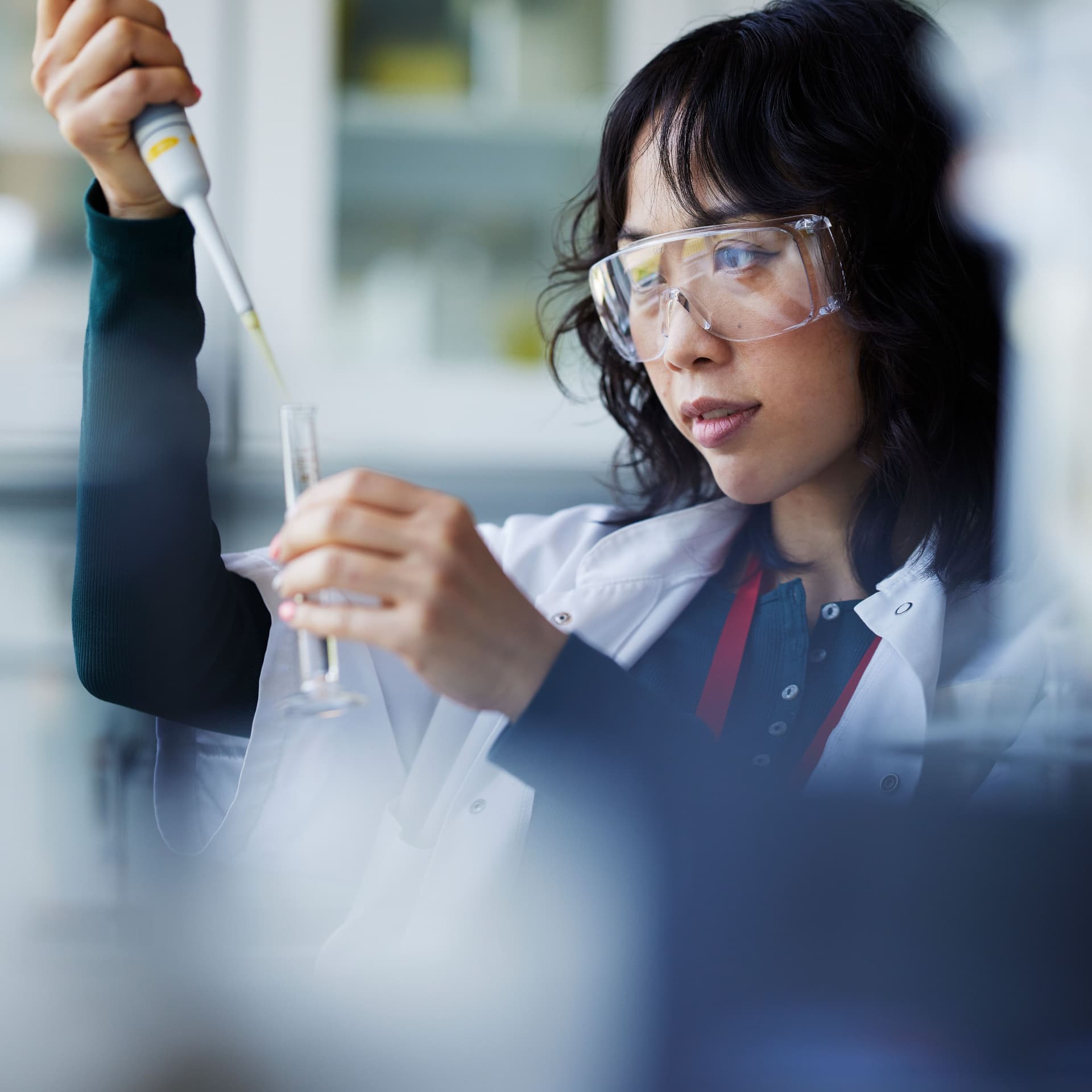 Eine junge Asiatin steht in einem Labor und forscht. Der Vordergrund ist unscharf.