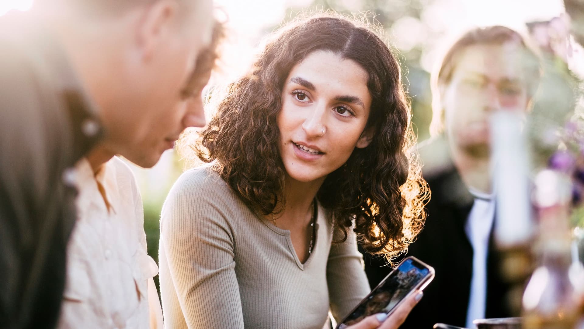 Junge Frau, die Freunden auf einer Gartenparty, Bilder in ihrem Smartphone zeigt.
