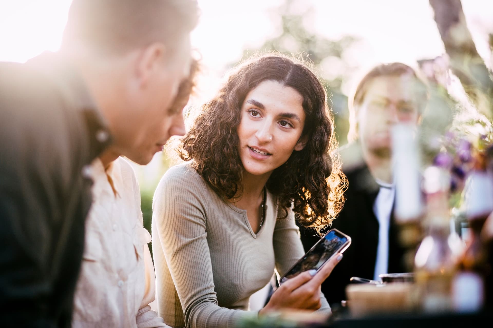 Junge Frau, die Freunden auf einer Gartenparty, Bilder in ihrem Smartphone zeigt.
