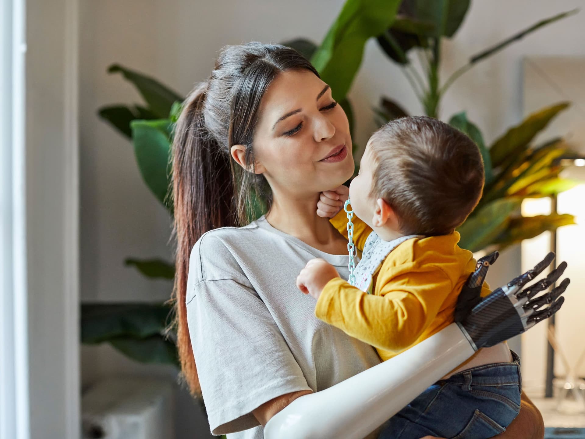 Eine junge Frau mit Armprothese hält ihr kleines Kind auf dem Arm. Sie lächelt.