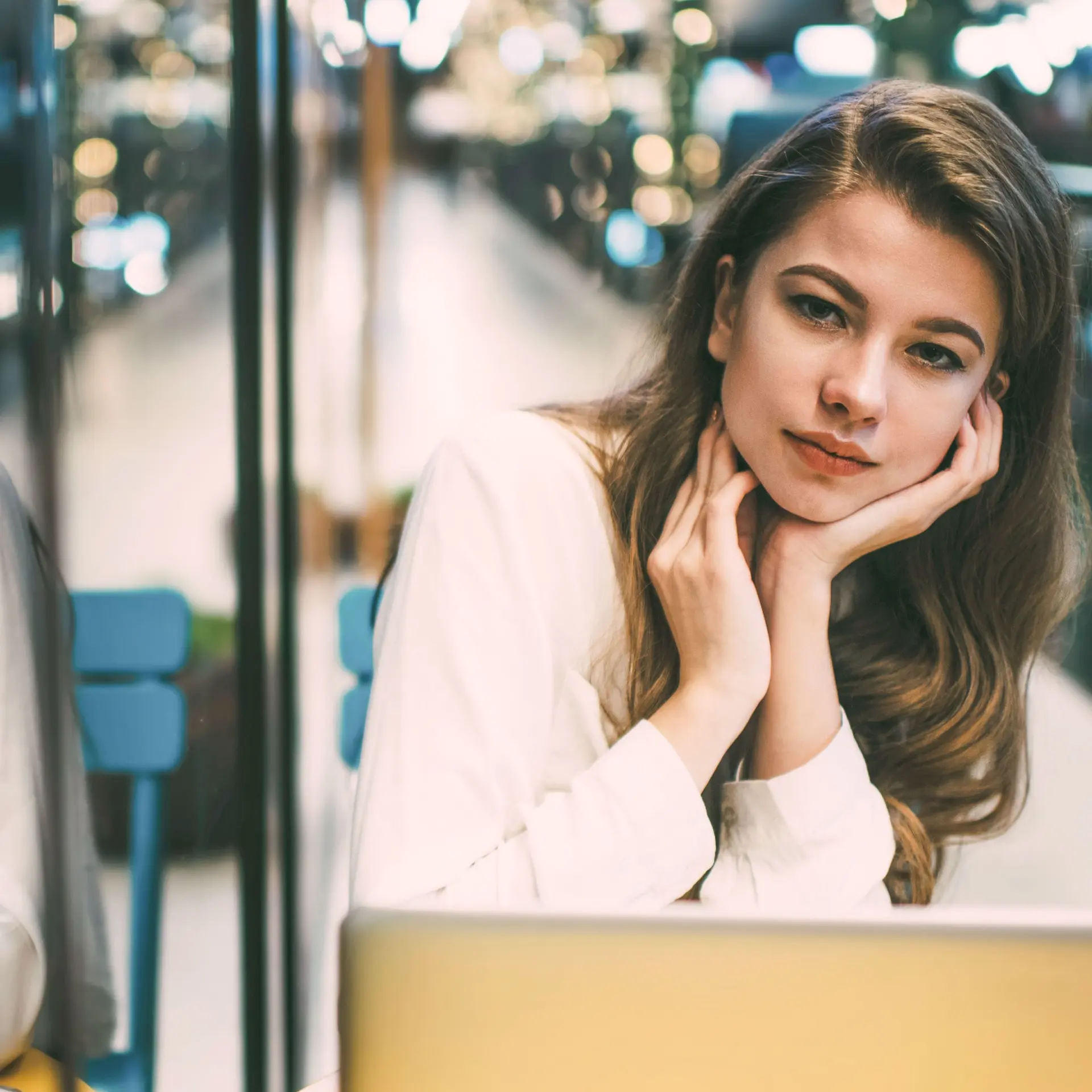 Porträt einer jungen Frau mit Laptop, die in die Kamera schaut. Links spiegelt sie sich in einer Glasscheibe.