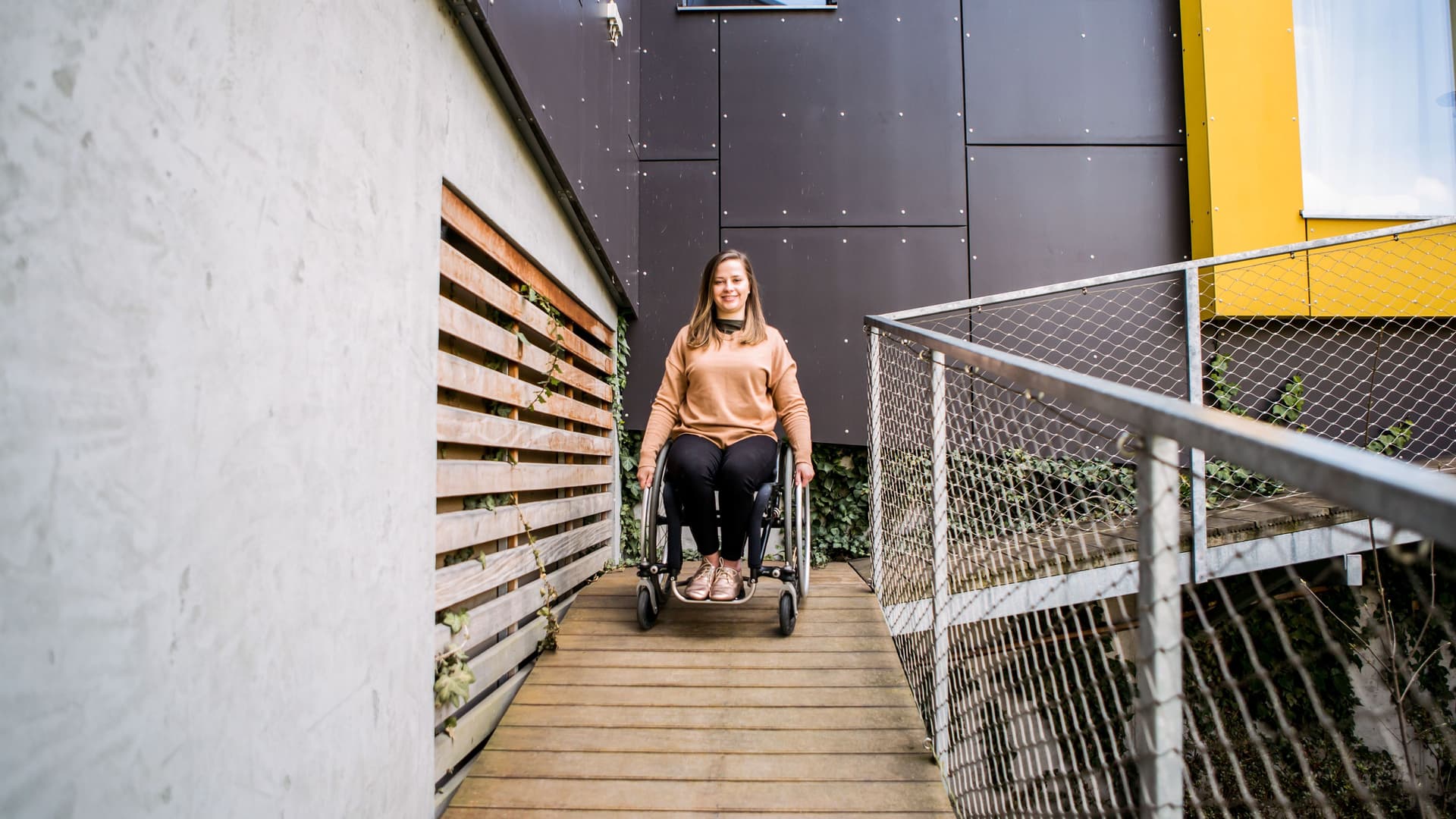 Junge Frau im Rollstuhl, die eine Rampe runterfährt.