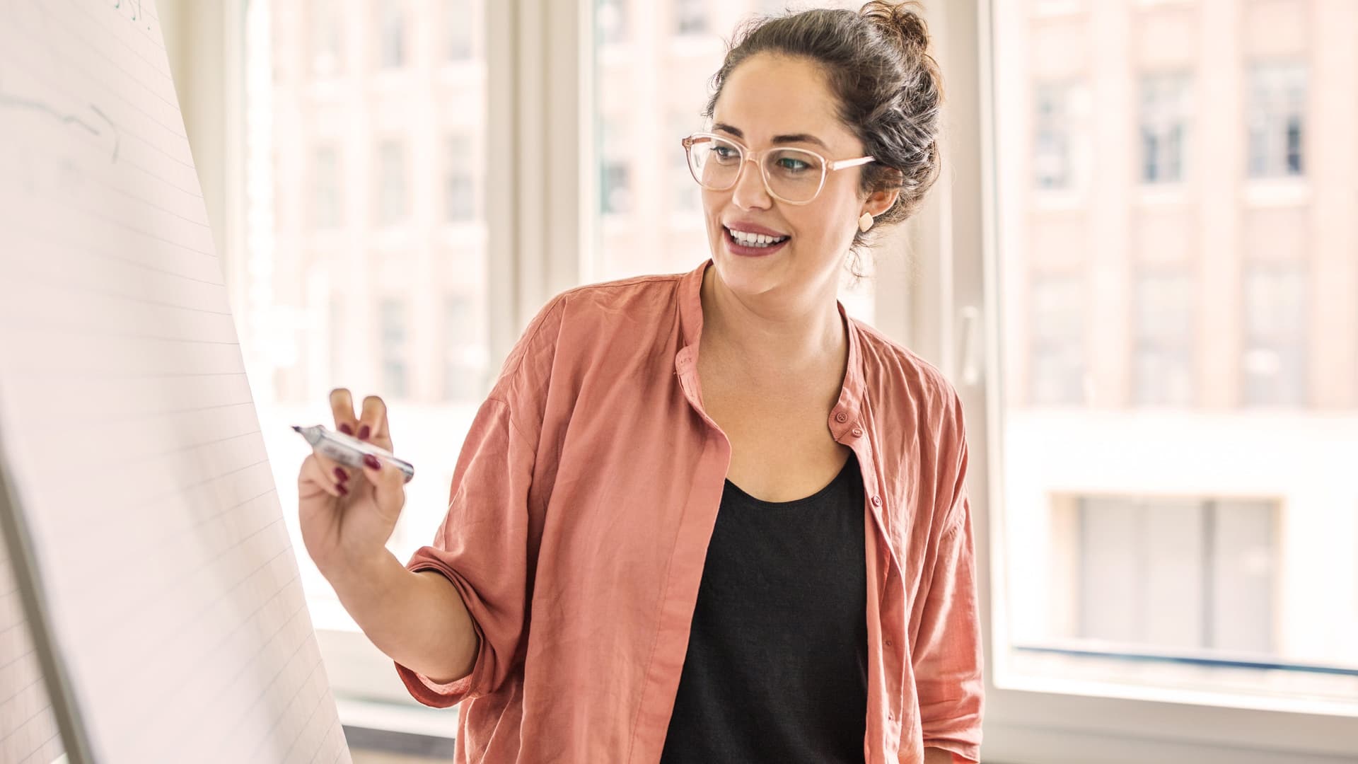 Junge Frau schreibt während einer Präsentation auf ein Flipchart. Sie lächelt dabei.