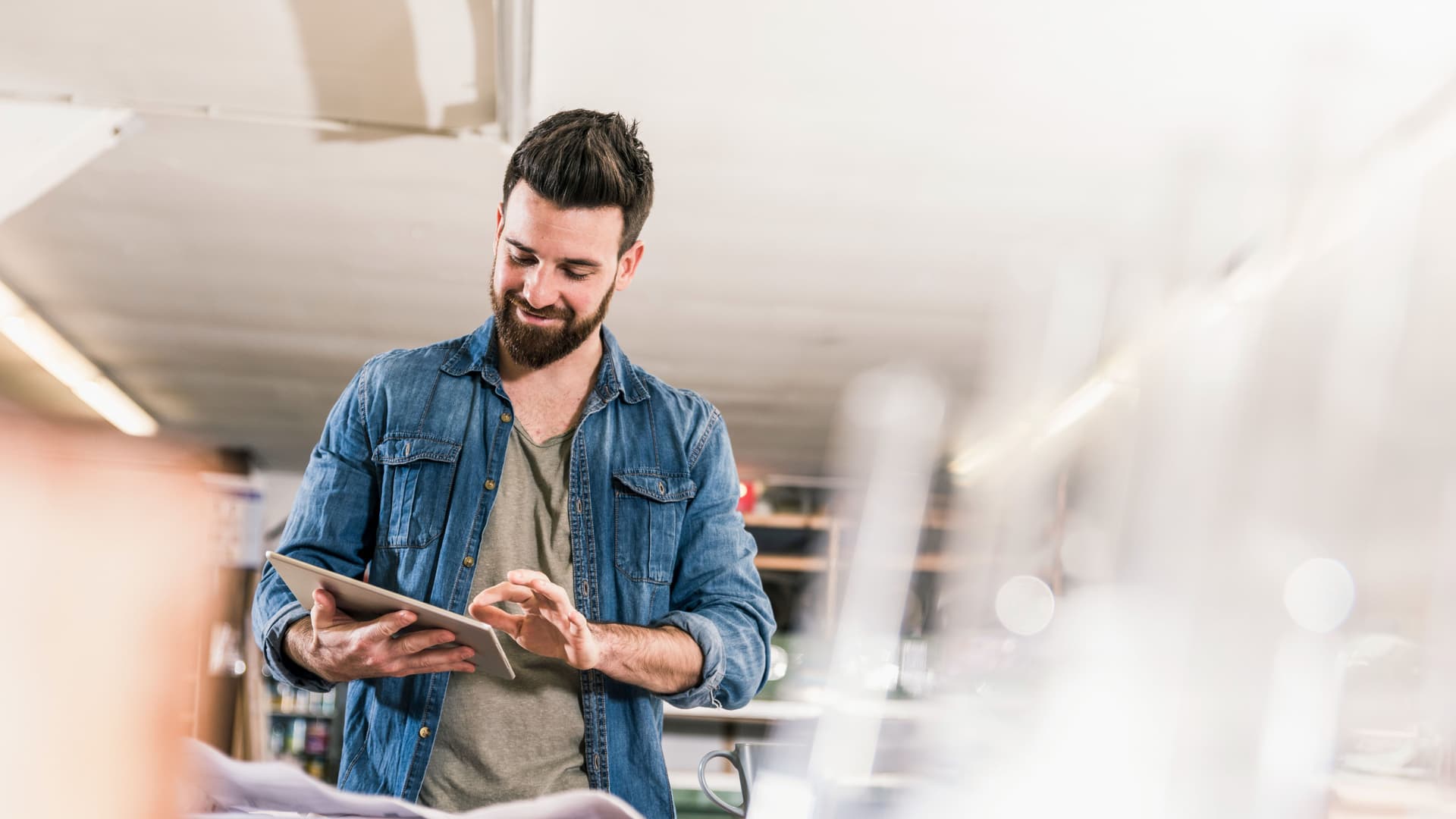 Lächelnder junger Mann tippt auf ein Tablet in einer Werkstatt.