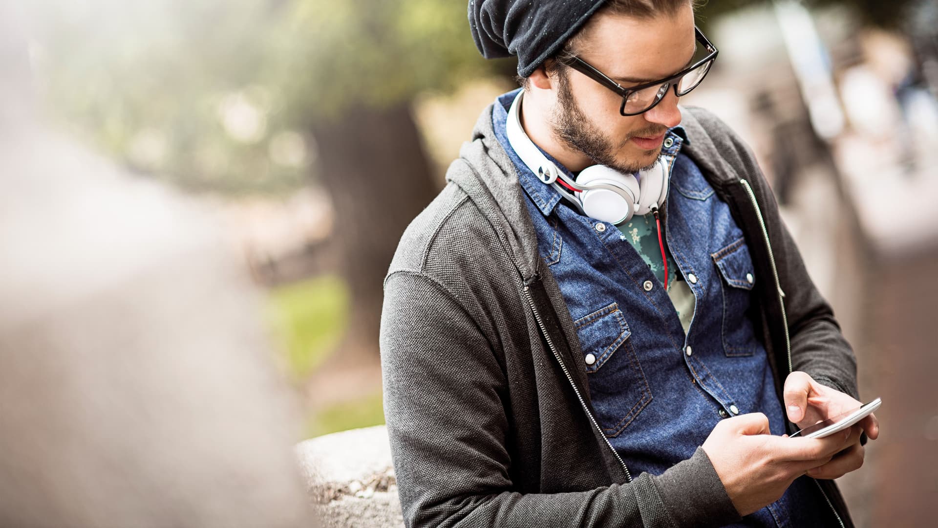 Junger Mann mit Mütze und Kopfhörern tippt auf einem Smartphone.