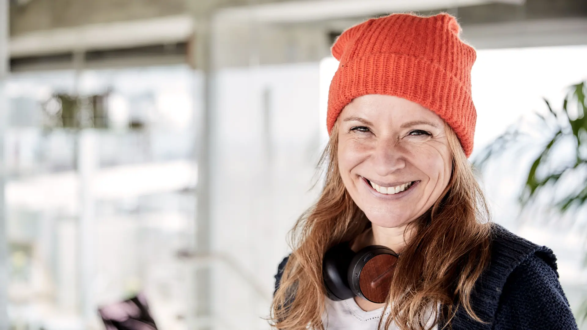 Mit 64 Jahren: Früher in Rente gehen und trotzdem arbeiten Lächelnde ältere Frau mit orangefarbener Wollmütze und Kopfhörern um den Hals.