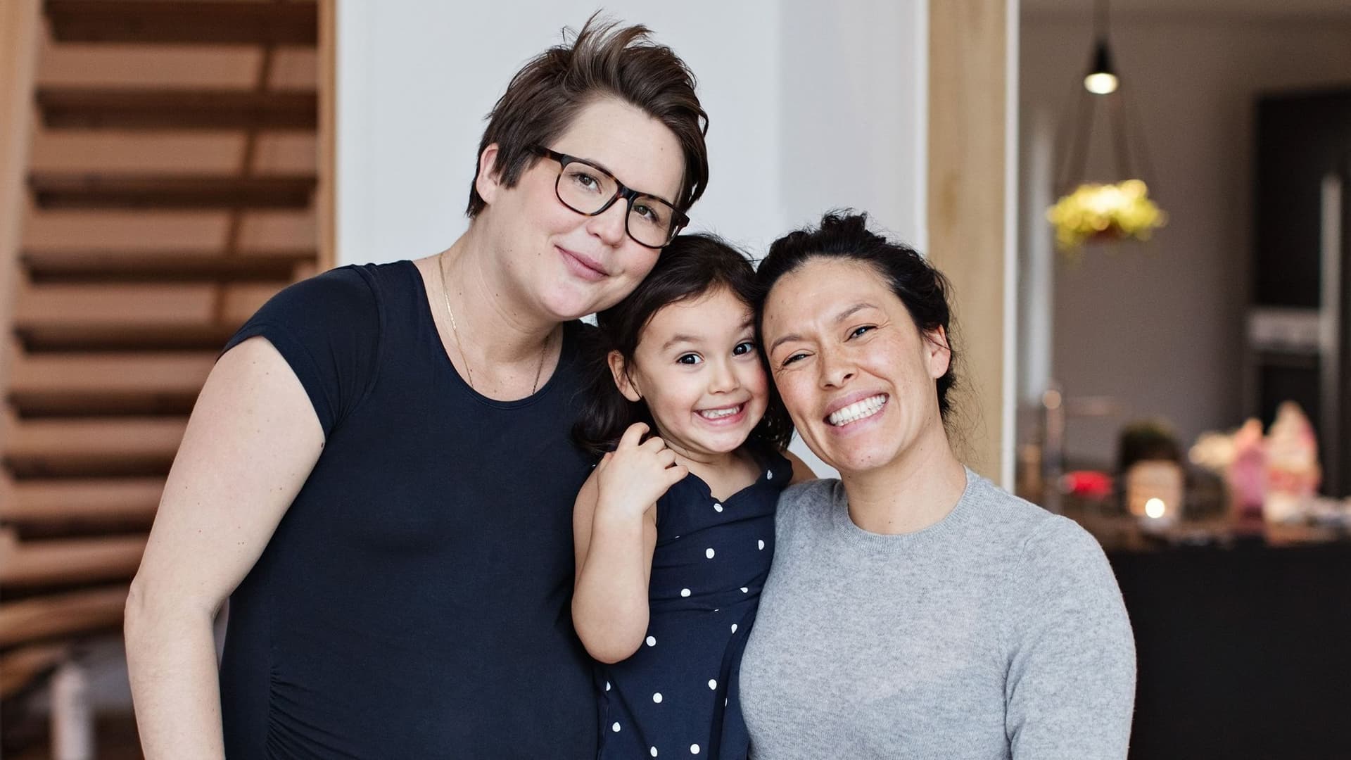 Porträt eines lächelnden lesbischen Paares mit Tochter im heimischen Wohnzimmer