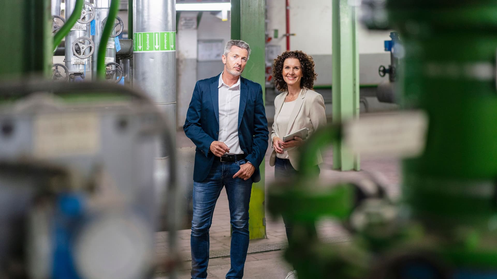 Lächelnde Geschäftsfrau mit Tablet in der Hand und Mann, die in einer Werkstatt stehen und in die Kamera gucken.