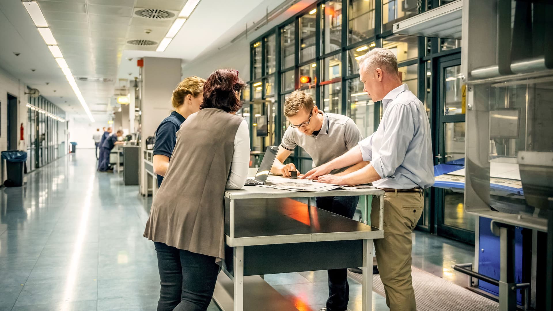 Personalversammlung mit verschiedenen Personen an einem Stehtisch in der Nähe einer Produktionshalle.