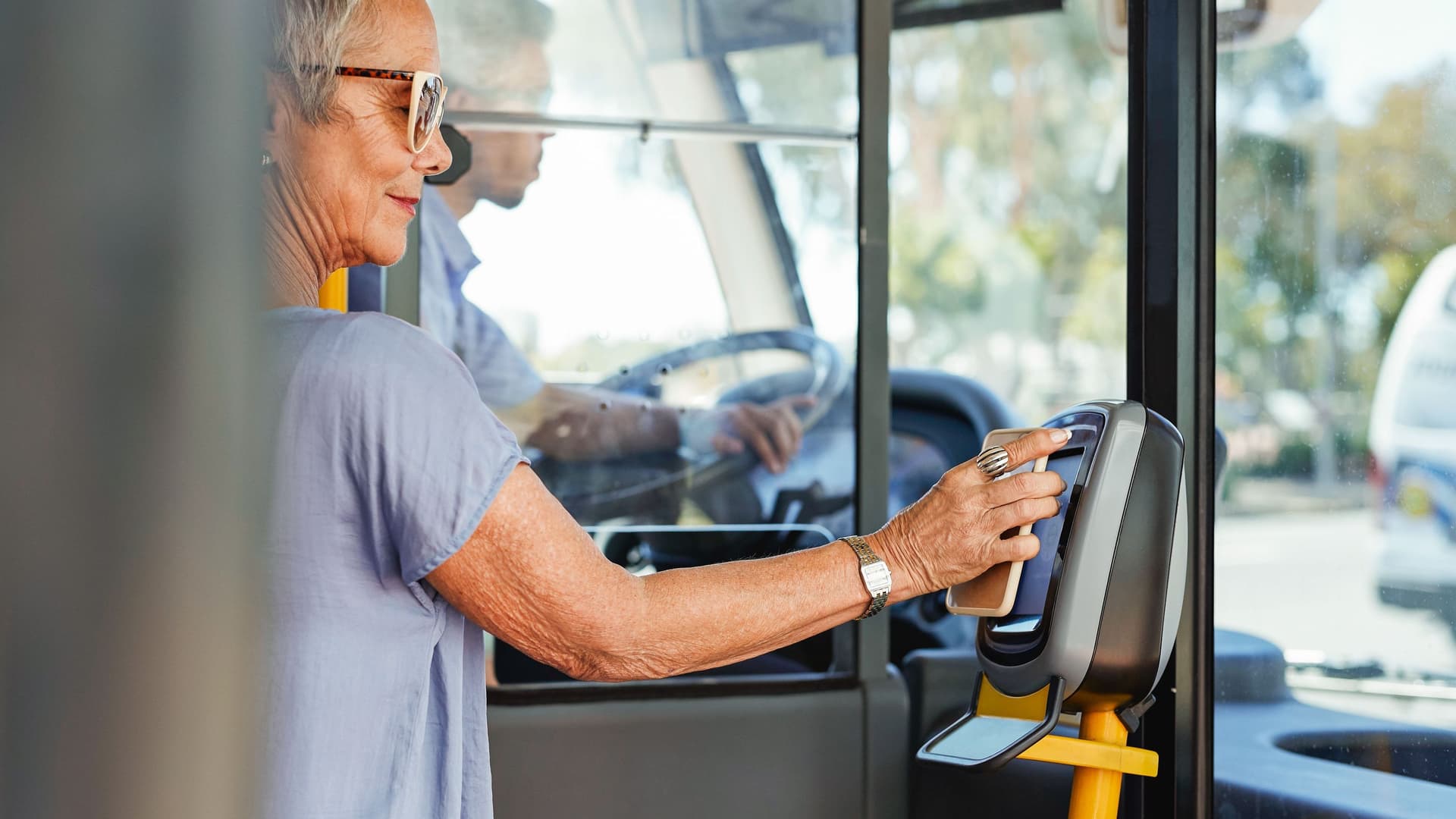 Mobile Payment Eine Seniorin steht im Einstiegsbereich eines Busses und bezahlt mit ihrem Smartphone am Lesegerät.