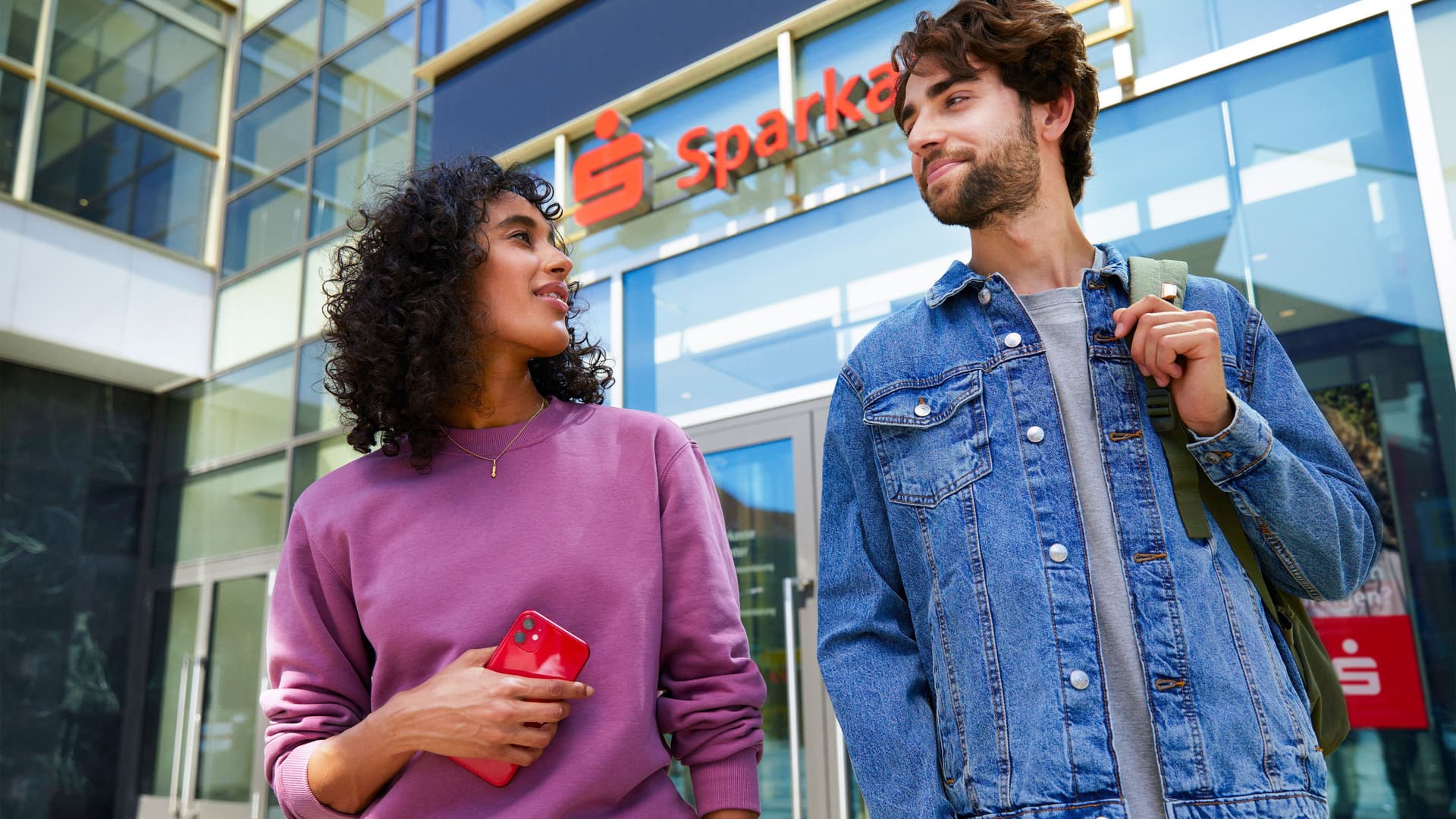 Junge Frau und junger mann gucken sich an am Eingang einer Sparkassen Filiale