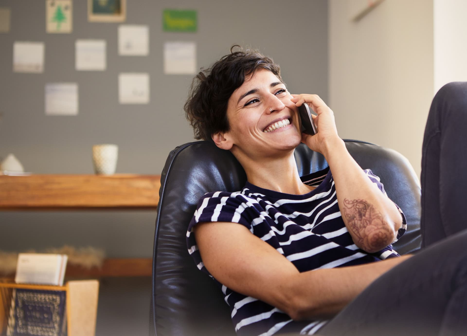 Junge lachende Frau sitzt telefonierend in einem Ledersessel