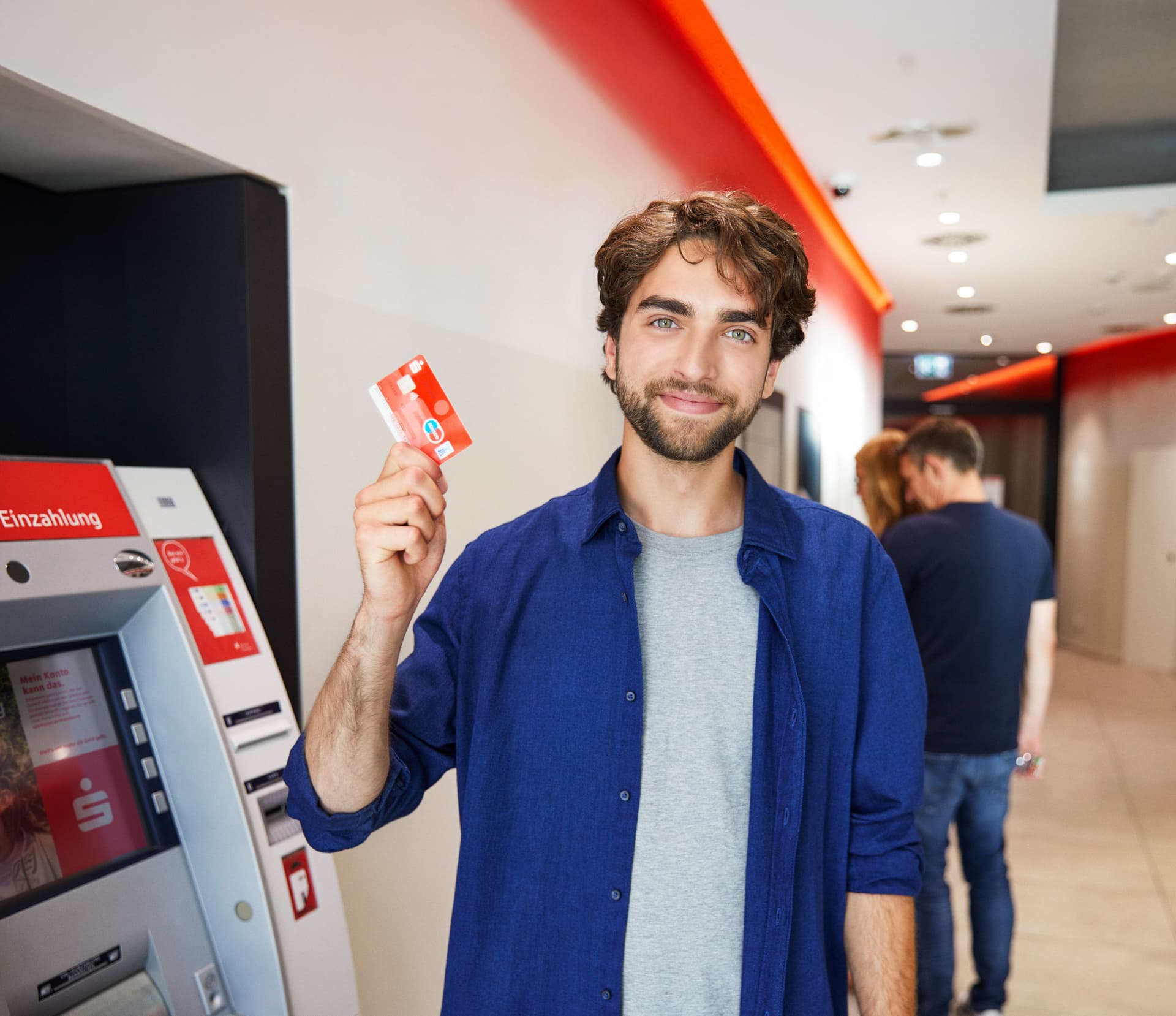 Junger erwachsene zeigt seine Sparkassen EC Kart neben einen Bankautomaten in einer Sparkassen Filiale