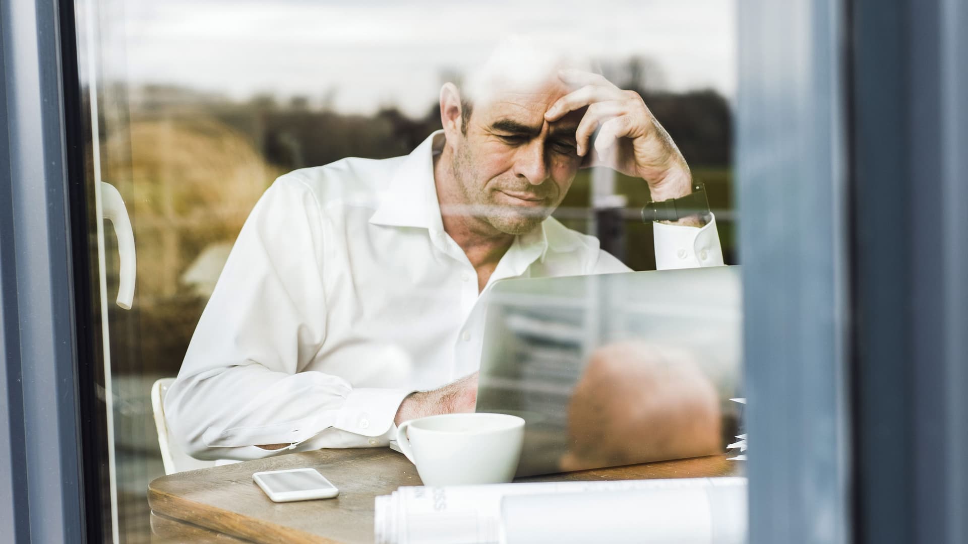 Geschäftsmann mit Laptop arbeitet am Holztisch beim Fenster