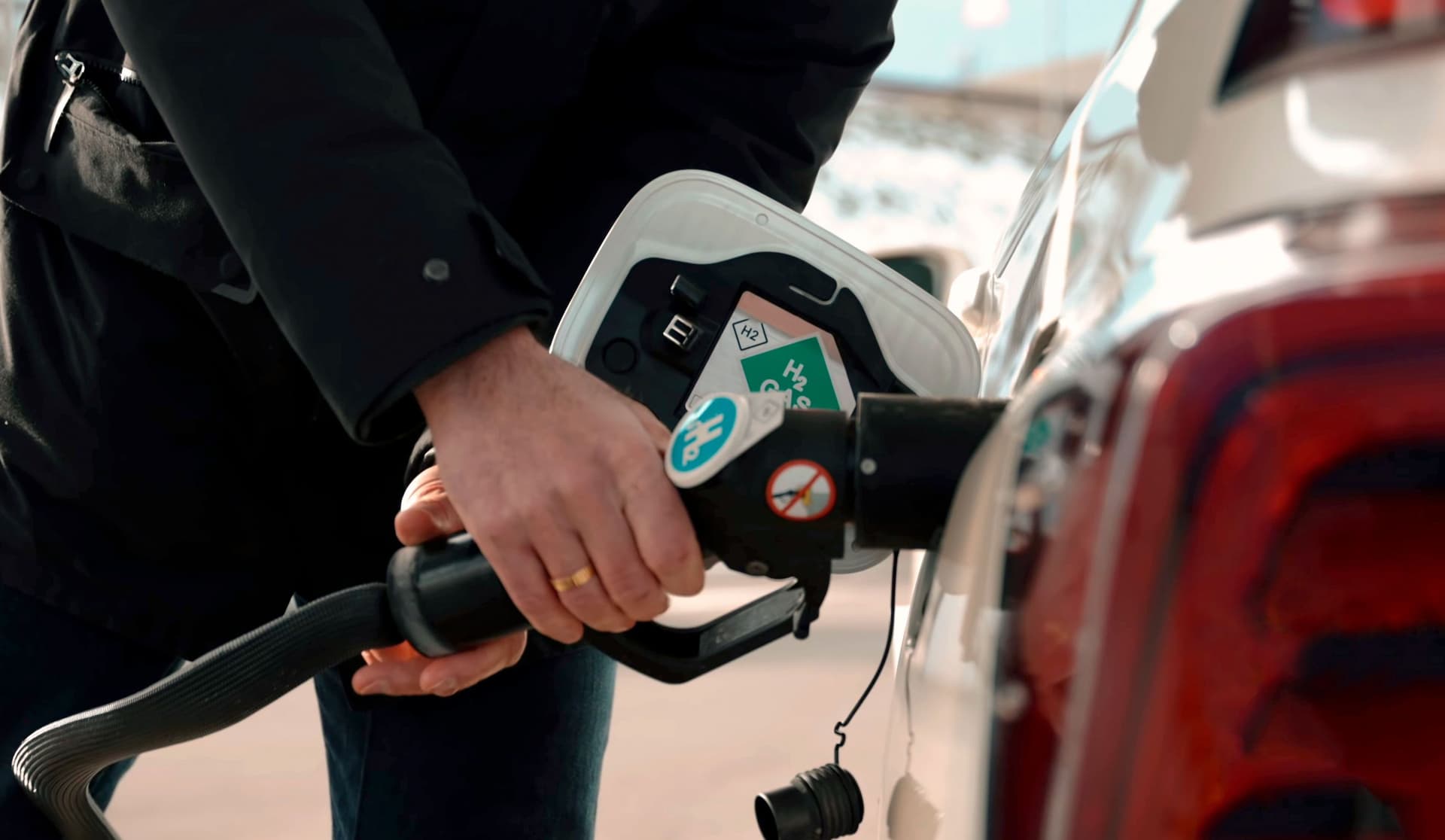 Nahaufnahme von Hände eines Mannes, der mit einem Einfüllstutzen sein Wasserstoff-Brennstoffzellenauto betankt.