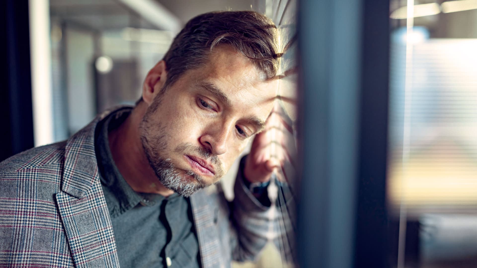 Geschäftsmann lehnt seinen Kopf an einer Scheibe und schaut ausgelaugt auf den Boden