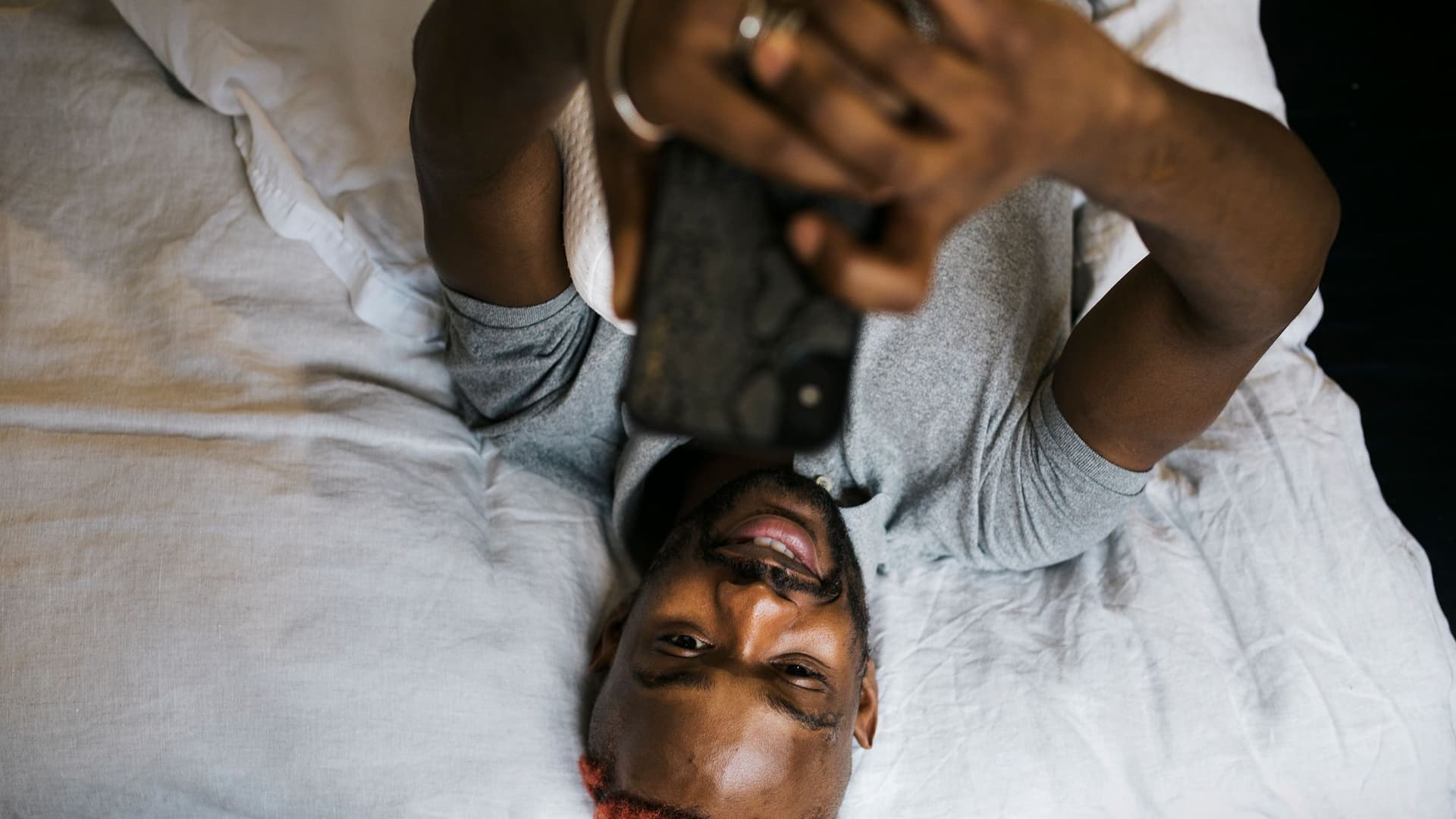 Mann liegt im Bett mit Handy in der Hand von oben