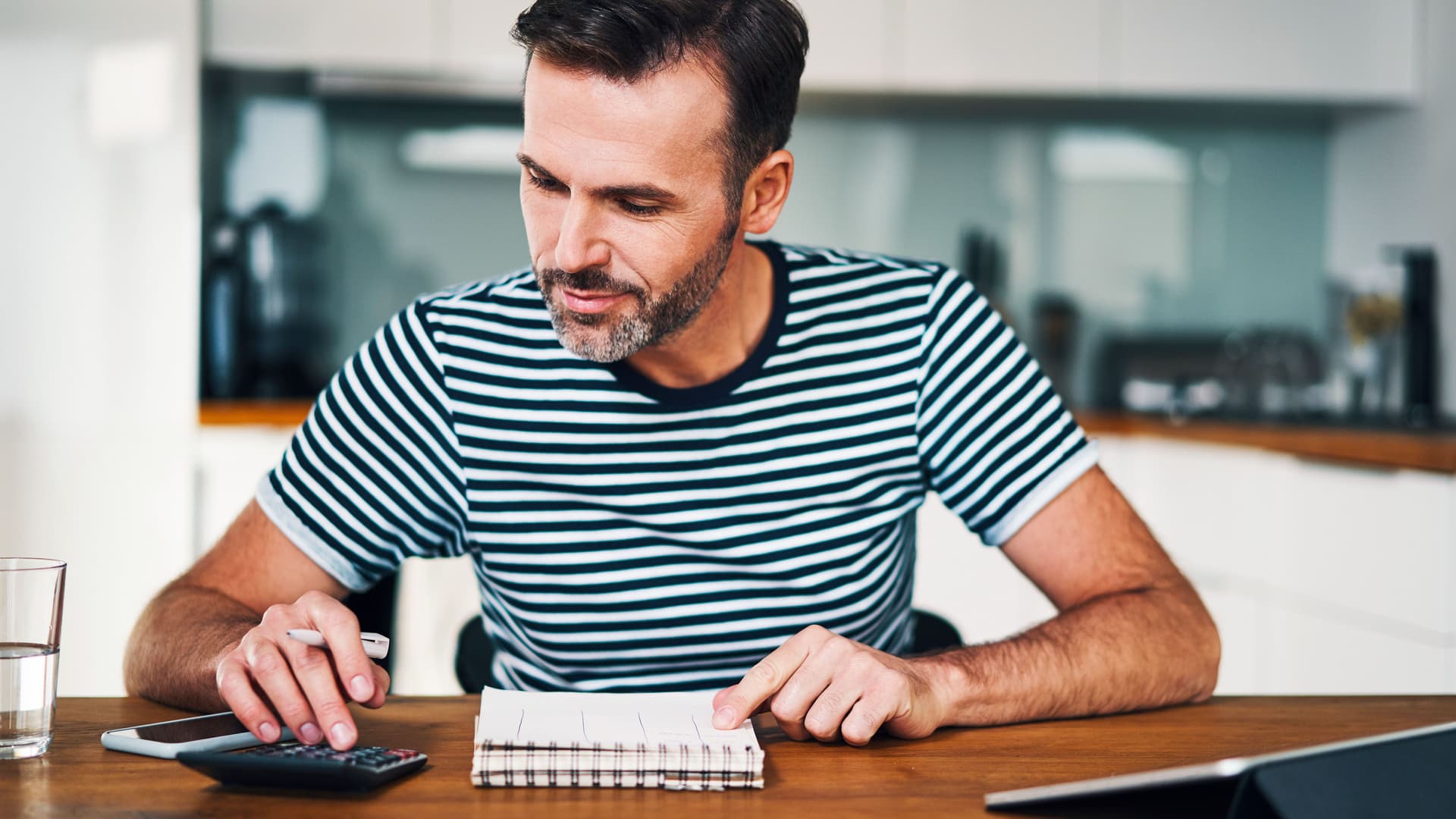 Mann verwaltet das Haushaltsbudget mit Taschenrechner, und Tablet Notizbuch am Esstisch.