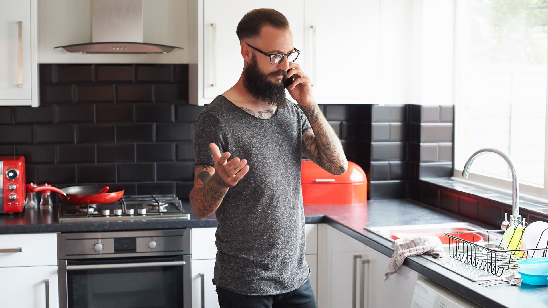 Mann steht in der Kueche und telefoniert mit seiner Versicherung nach Einbruch.