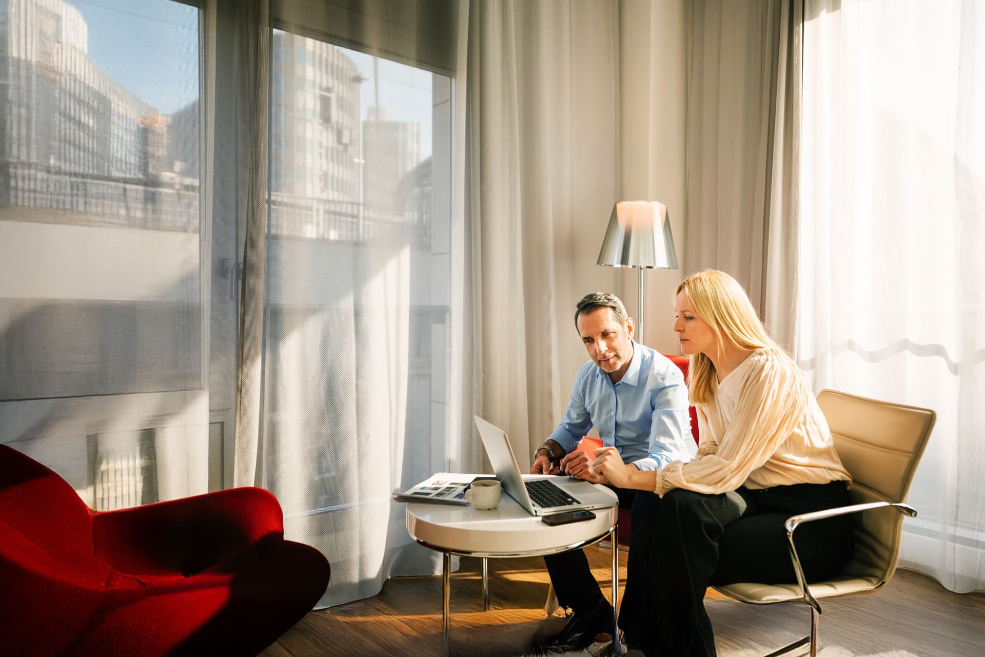 Zwei Kollegen arbeiten gemeinsam am Laptop in einem Hotelzimmer.