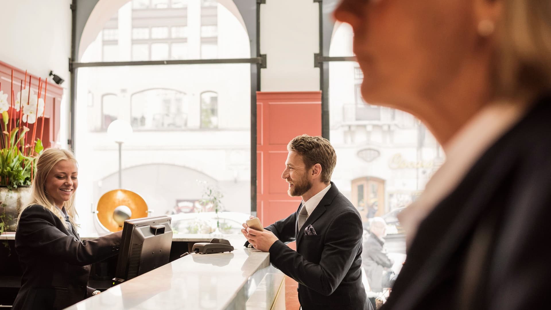 Ein Mann unterhält sich lachend an einer Hotel-Rezeption mit einer Hotelangestellten.