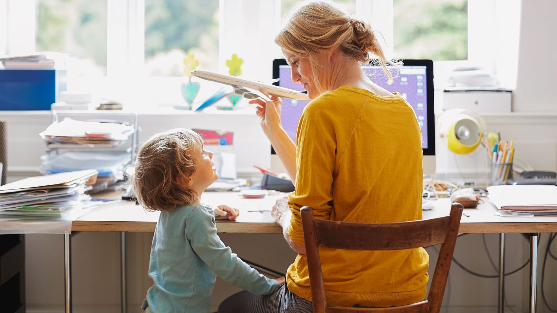 Frau am Schreibtisch zeigt Kind ein Modellflugzeug