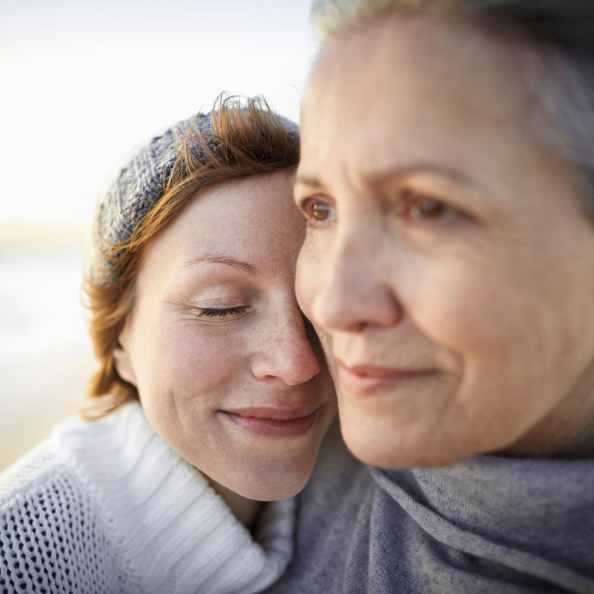 Mutter und erwachsene Tochter am Strand. Sie umarmen sich.