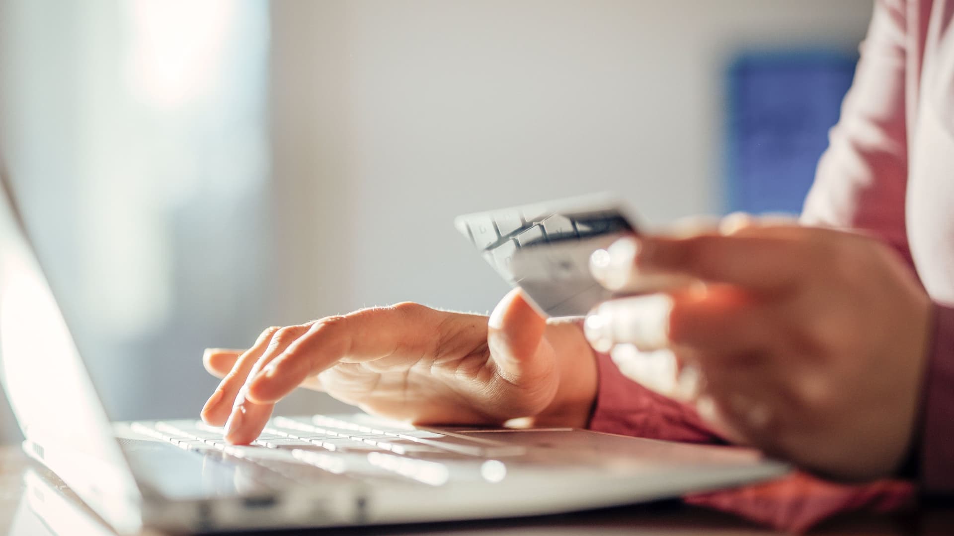 Nahaufnahme einer Frau vor einem Laptop die eine Bankkarte in der Hand hält.