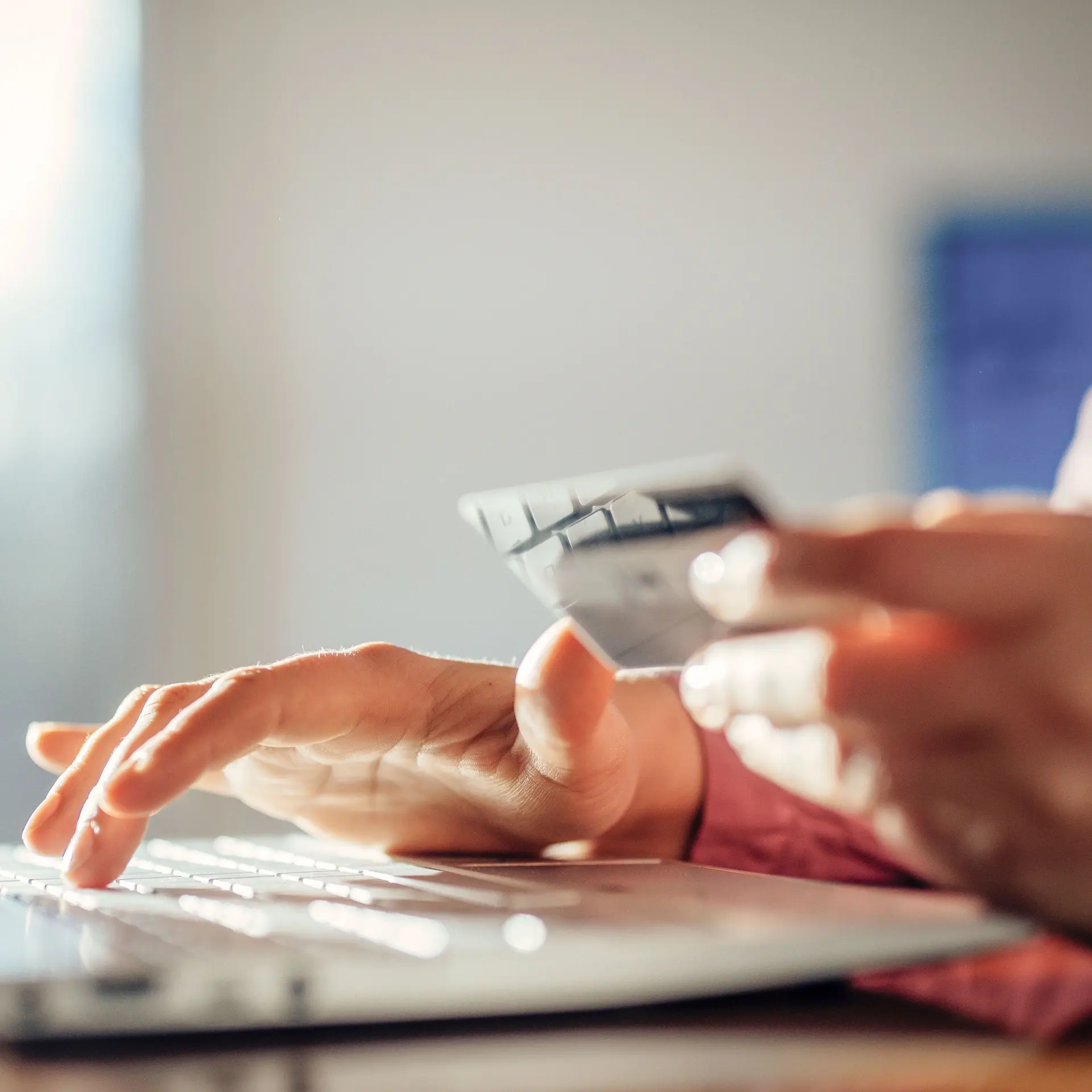 Nahaufnahme einer Frau vor einem Laptop die eine Bankkarte in der Hand hält.
