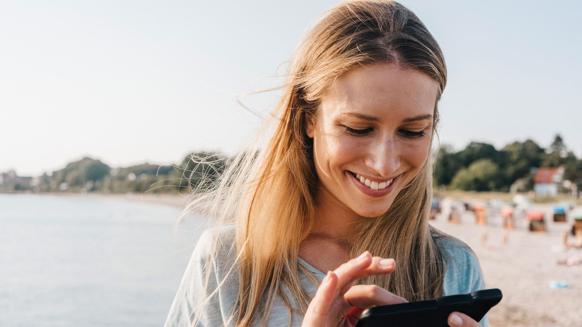 Eine junge Frau steht am Strand und benutzt ihr Smartphone