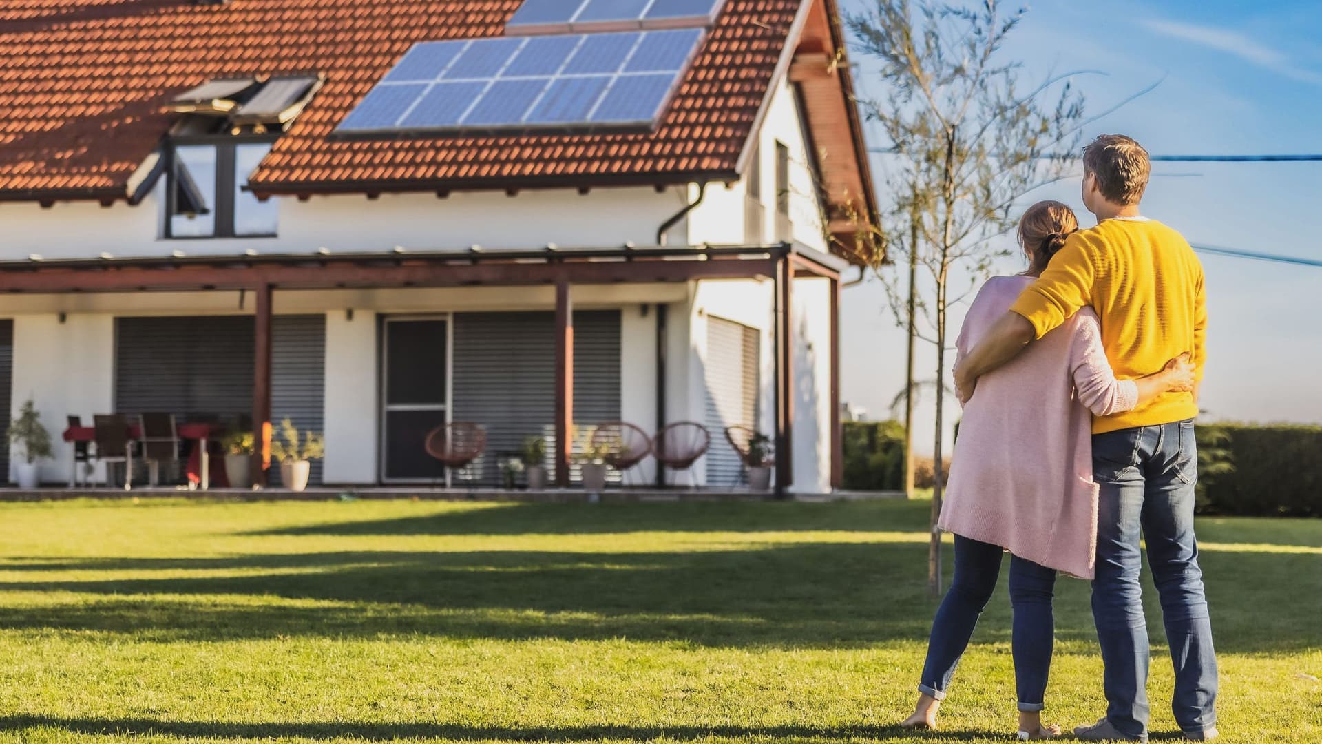 Ein Paar steht auf einer Wiese und blickt auf ein Einfamilienhaus mit Solaranlage