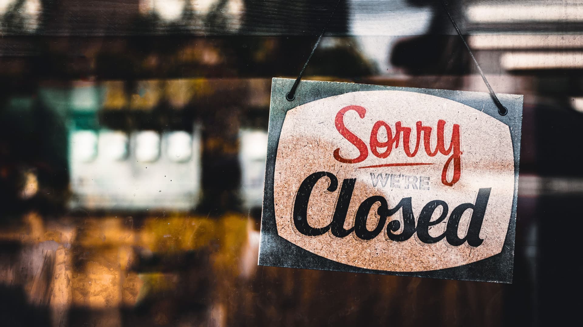 Schild mit der Aufschrift "Sorry we're closed" hängt hinter einer Glasscheibe von einem Laden.