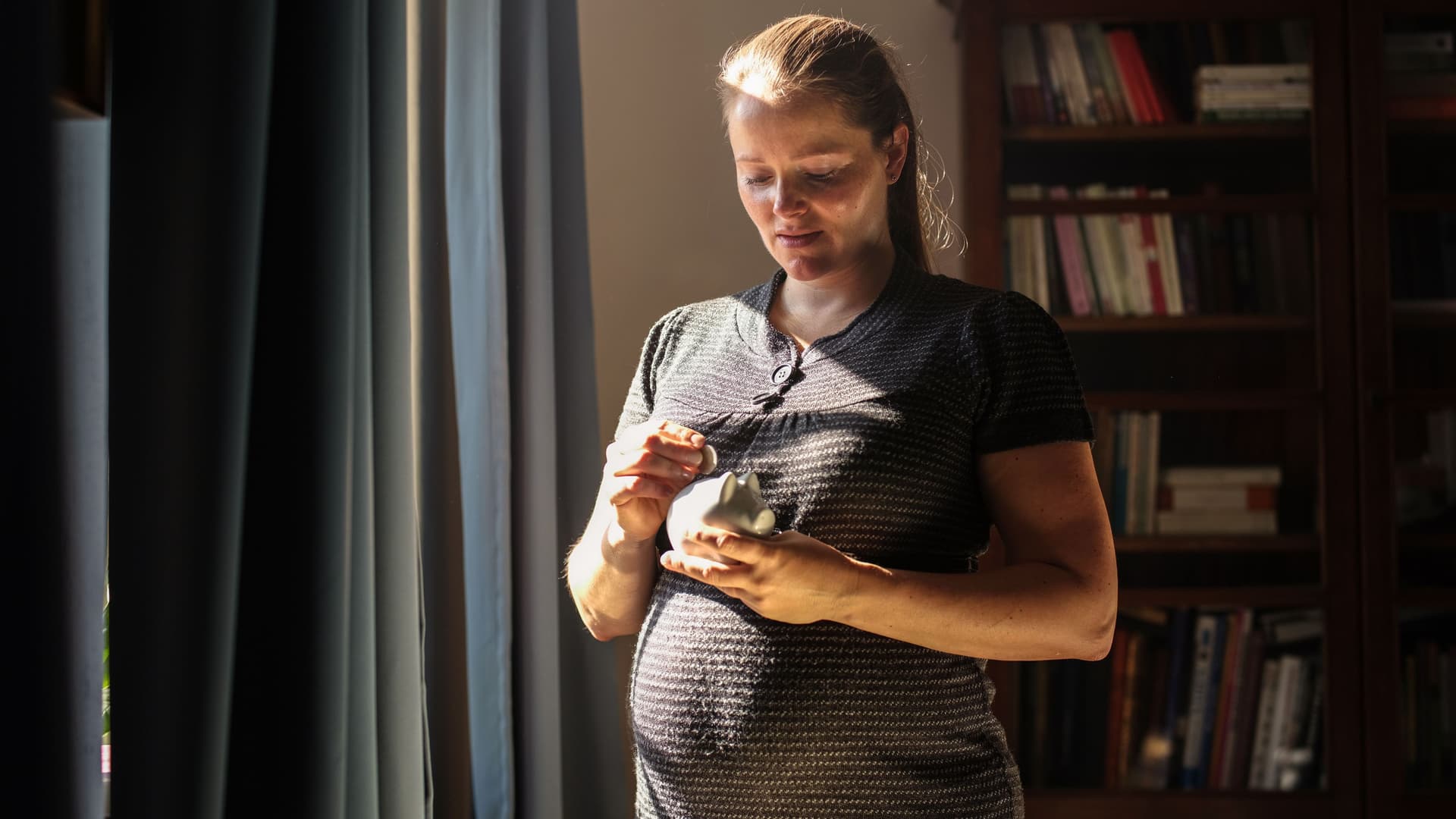 Schwangere Frau, die zu Hause eine Münze in ein Sparschwein steckt.