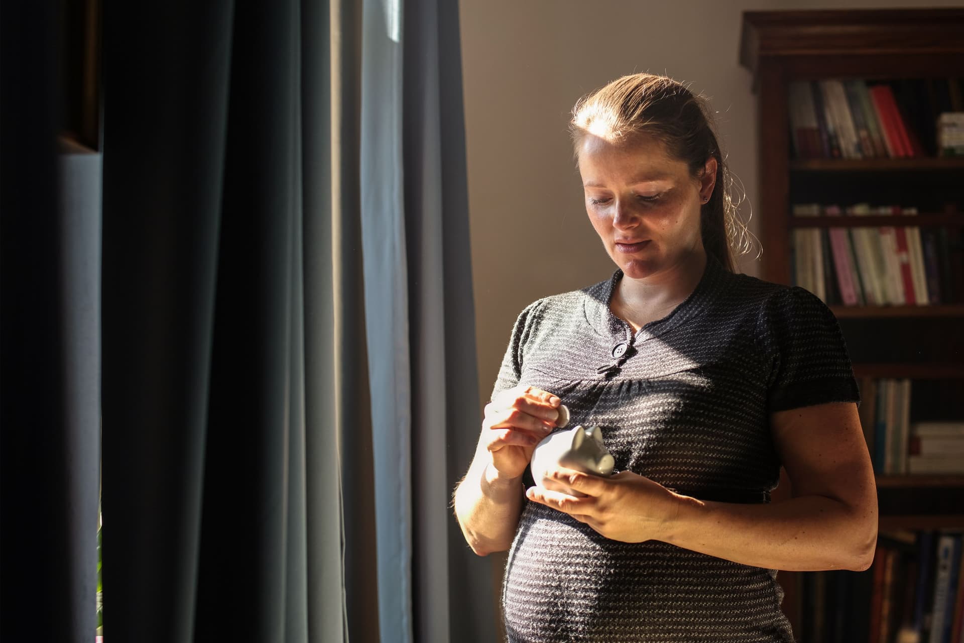 Schwangere Frau, die zu Hause eine Münze in ein Sparschwein steckt.