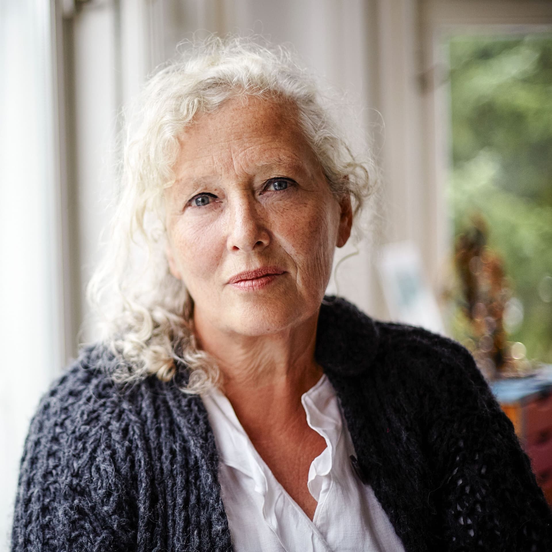 Porträt einer älteren Frau zu Hause die ernst in die Kamera schaut.