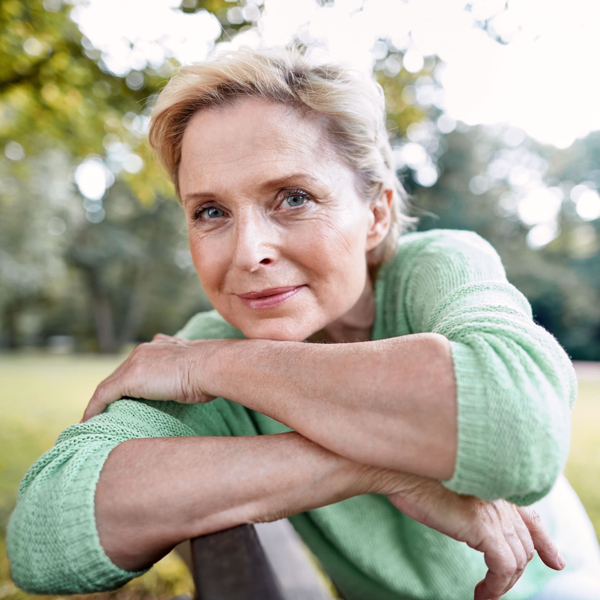 Porträt einer reiferen Frau, die sie an eine Parkbank lehnt und in die Kamera schaut.