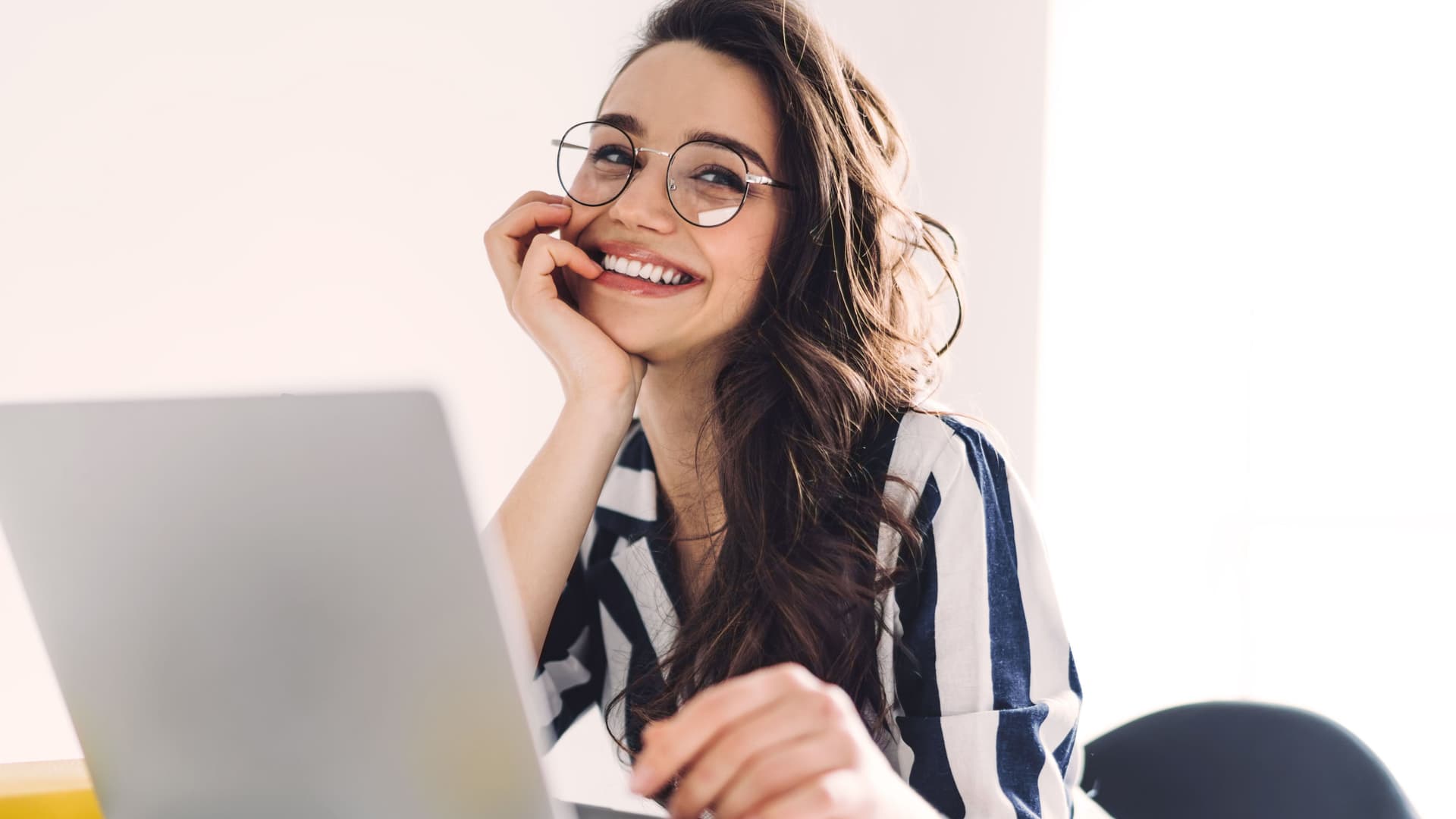 So erkennen Sie seriöse Online-Händler Junge Frau lächelt Richtung Kamera. Sie sitzt am Schreibtisch vor einem Laptop.