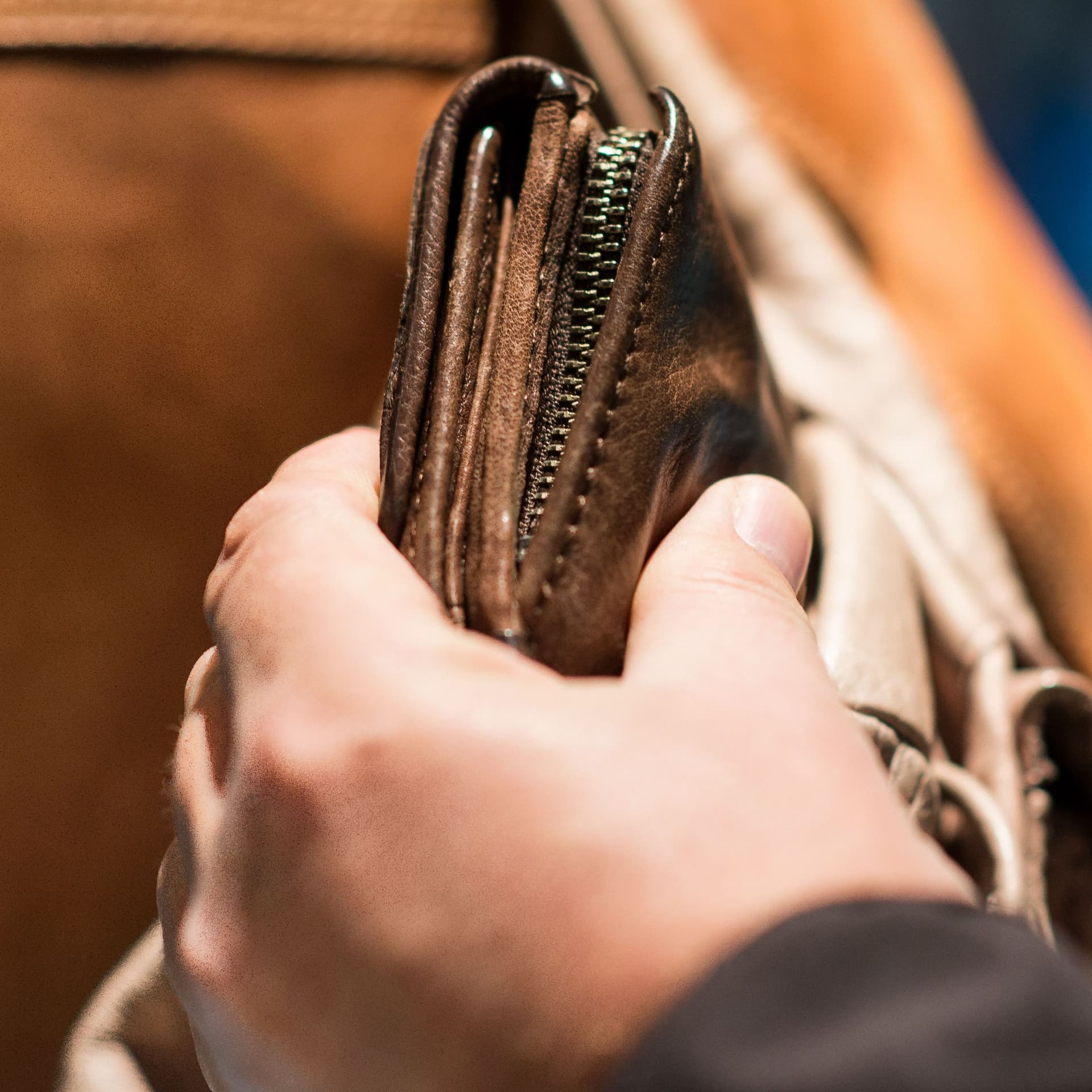 Jemand entwendet ein Portemonnaie aus einer braunen Tasche.
